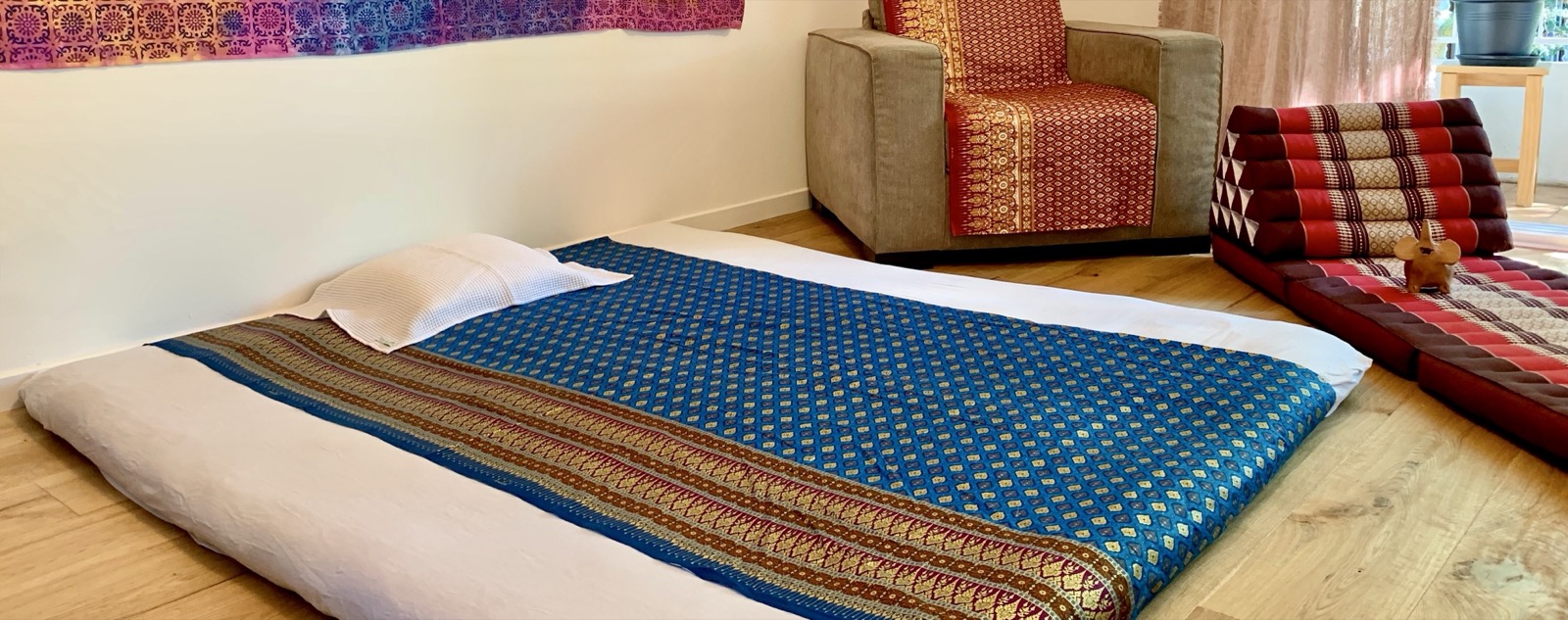 Vue d'ensemble du cabinet : futon de massage au sol et tentures thaïlandaises